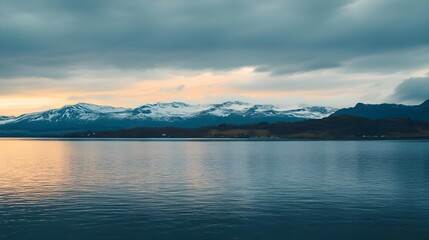 Serene landscape of mountains and water under a cloudy sky at dusk, capturing the beauty of nature's calmness.