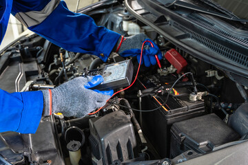 Car mechanic man with voltmeter checking battery during car maintenance in auto repair service