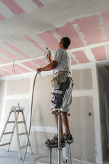 The worker make a plasterboard ceiling. He does spraying gypsum putty  to the plasterboard joints....
