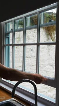 Vertical video social media - Closeup of a man&rsquo;s hands raising a traditional sash window to open it in a kitchen.