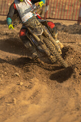 A motocross rider bending his bike into a tight turn on a wet dirt track illuminated by the evening...