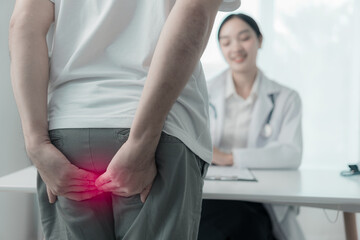 Fototapeta premium A young man with hemorrhoids is consulting a doctor. Man touches her butt because of stomach pain and hemorrhoids Health care concept People with hemorrhoids