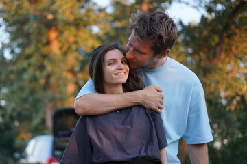 Fototapeta premium woman in a black shirt embraces a man in a blue shirt as they stand in a forest. The sun shines behind them, creating a warm, golden glow