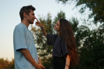 woman playfully jokes with her partner, who is bent over with laughter, while standing in a park on...
