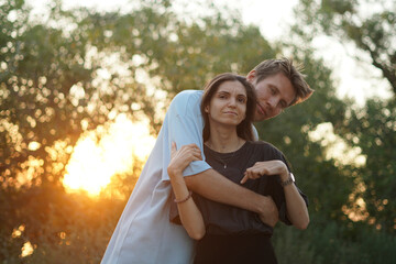 Fototapeta premium man and woman stand close to each other in a forest during sunset, the sun shining brightly behind the trees