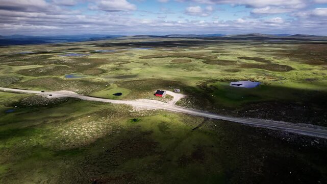 Aerial Orbit Shot: car traveling along Sweden's highest country road Flatruetv&auml;gen, passing an old red barn against the vast, barren landscape of Flatruet high fell plateau and mountains
