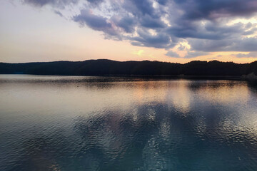 A serene sunset over a tranquil lake, reflecting colorful clouds and surrounding trees in the water