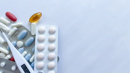 Assortment of multicolored pills, capsules, and a digital thermometer showcasing a normal temperature, set against a clean white background, ideal for health and medical use