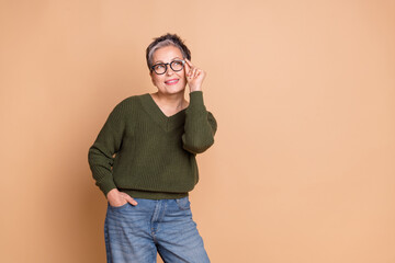 Photo of smart woman with short hairdo dressed khaki sweater touch glasses look at sale empty space isolated on beige color background