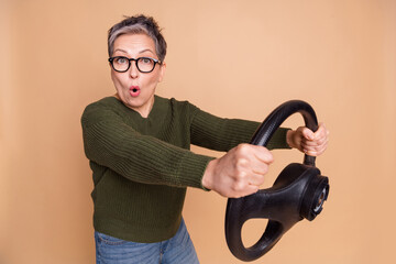 Photo of shocked retired woman wear green stylish clothes drive new speed car isolated on beige color background