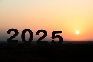 "2025" silhouetted against a desert sunrise, featuring a vibrant yellow-orange sky with plenty of copy space, perfect for conveying themes of challenge, business, and personal motivation