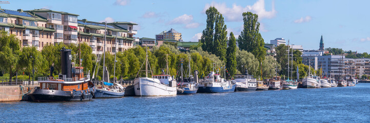 The harbor and piers with old fishing and tug boats in the bay Hammarbysjö, apartment houses,  a sunny summer day in Stockholm