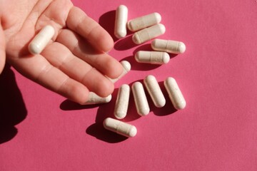 A child's hand holding a pill on a pink background. Medications. Concept: successful treatment, recovery. Vitamins. 