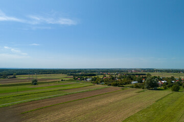 A beautiful aerial view showcasing lush green fields and a serene village under a clear blue sky,...