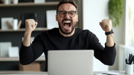 A man expressing excitement with raised fists at his workstation after achieving a significant milestone in his work. Sunlight filters through large windows, creating an inspiring atmosphere