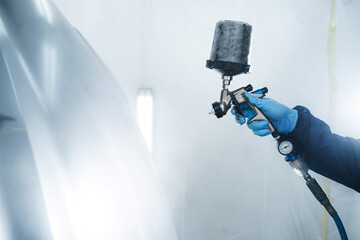 Car painter is using HVLP or LVLP spray gun to apply paint on metal. Painting cars in vehicle...