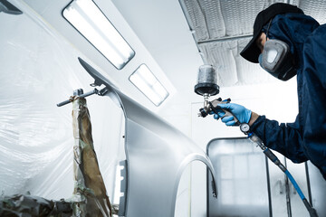 Worker is painting car in dark color with HVLP spray gun. Auto mechanic is changing the color of vehicle using sponge and paint sprayer.