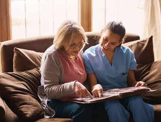 Elderly, woman and nurse with photo album in home for memories, nostalgia and remember with...