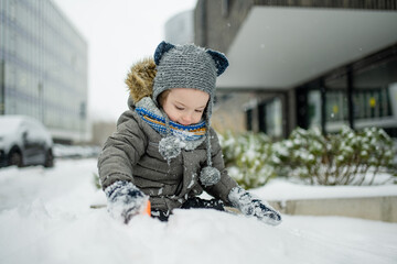 Adorable little boy having fun in a city on snowy winter day. Cute child wearing warm clothes playing in a snow.