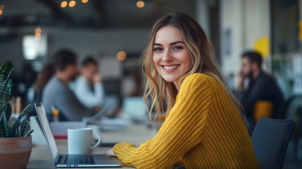 A young woman in a yellow sweater is sitting at a desk with a laptop and a coffee mug, smiling and looking away from the camera while her co-workers work behind her