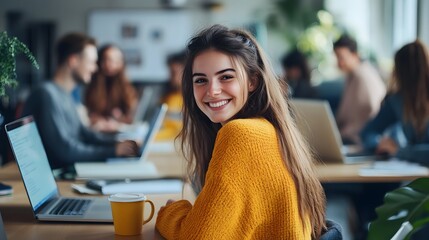 A young woman in a yellow sweater is sitting at a desk with a laptop and a coffee mug, smiling and looking away from the camera while her co-workers work behind her