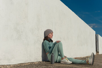 Sporty woman sitting resting after exercise outdoors, white wall background.