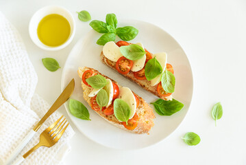 Bruschetta toasts with mozzarella, cherry tomato and basil leaves on white wooden table