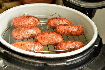 Fried sausages lie on the grill in a multicooker, side view.