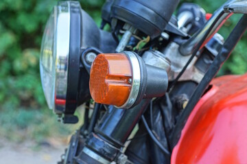 one small round red glass headlight turn signal on a old motorcycle on the street