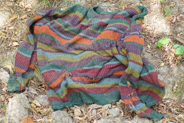 one old wrinkled colored wool striped dirty sweater lies on the gray ground on the summer street