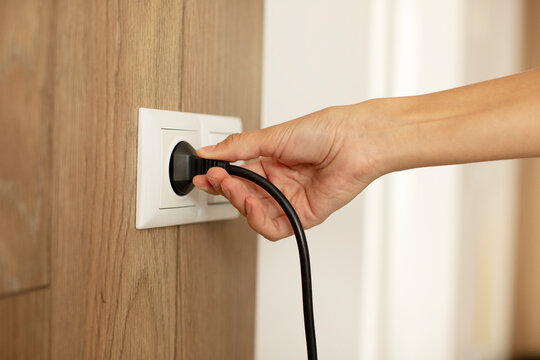 Woman putting on or removing electric plug cable in socket, closeup. Electrical equipment wires and power strips on the wall