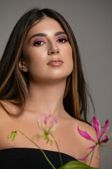 Fototapeta premium Closeup portrait of a beautiful young woman in a black dress with bare shoulders, posing in studio with a pink flowers.