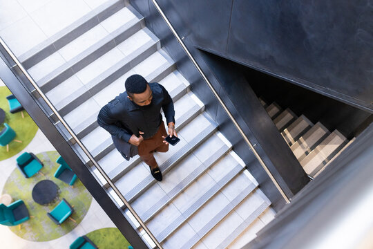 Walking up stairs, businessman holding smartphone and coffee cup in office building