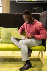 Smiling businessman using laptop while sitting on green sofa in modern office