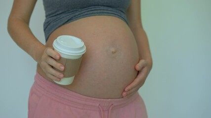 Closeup of a pregnant woman holding a cup of coffee, occasionally sipping. This video underscores the caution needed regarding caffeine intake during pregnancy, highlighting the importance of