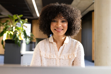 Working on laptop, smiling businesswoman in modern office environment