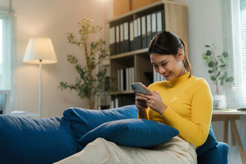 Young woman happily uses her smartphone in a cozy living room, enjoying a peaceful break with natural light