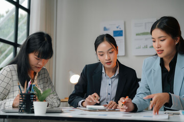 Young female entrepreneur using a calculator for calculations while her coworkers review documents