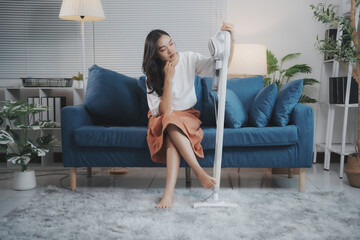 Tired woman procrastinating cleaning, sitting on couch, holding vacuum, looking bored in living room. Asian, long hair, casual clothes, barefoot