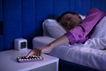Woman snoozing off alarm clocks on her cellphone, reaching hand to phone and lying down in bed at...
