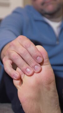Vertical view of a man checking his toes due to foot pain. Living room set. Shallow depth of field.  	