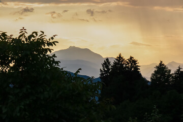 Fiery sunset over mountain summit Dobratsch in Rosental, Carinthia, Austria, Europe. Silhouette of forest and rolling hills in Austrian Alps. Vibrant orange and yellow hues. Tranquil serene atmosphere