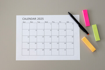 Blank calendar with 2025 writing and a pen and colorful note stickers on table. Space for text