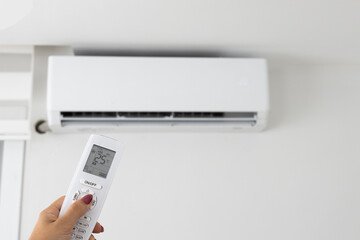 Adjusting air conditioner temperature with remote control. Hand holds remote control and setting...