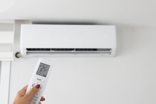 Adjusting air conditioner temperature with remote control. Hand holds remote control and setting comfortable temperature on climate system in apartment