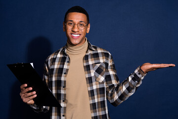 Photo of handsome good mood guy wear checkered shirt writing documents holding arm emtpy space isolated blue color background