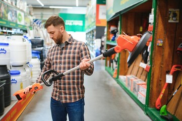 a young man in a gardening equipment store chooses an electric trimmer for mowing lawn grass