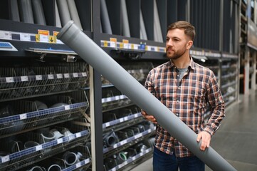 Handsome man choosing sewer pipes standing near the showcase of the plumbing shop