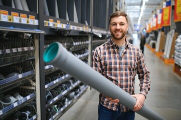 Handsome man choosing sewer pipes standing near the showcase of the plumbing shop