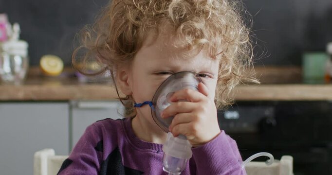 A child treats a respiratory disease with the help of inhalations. The child has a mask for home inhalations on his face, breathes and steam comes out of the mask.